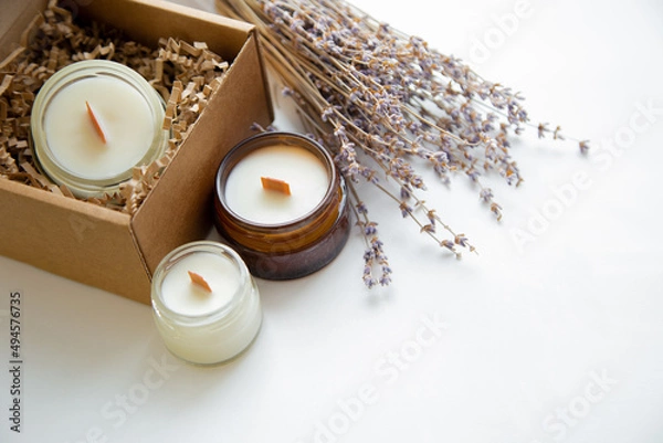 Fototapeta An open box with candles on a white background, next to it are several candles in a jar and a dried bouquet of lavender. High quality photo