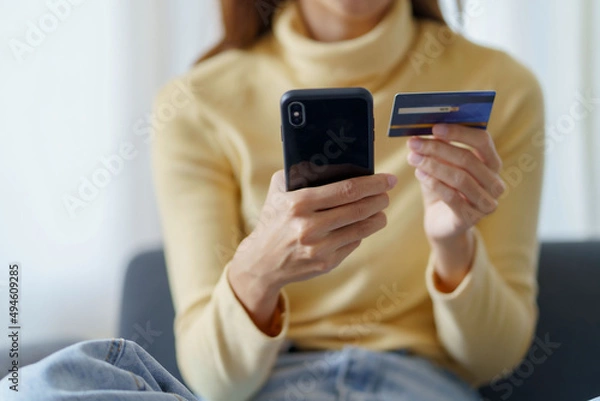 Fototapeta Young woman using smartphone and credit card for online shopping at home.