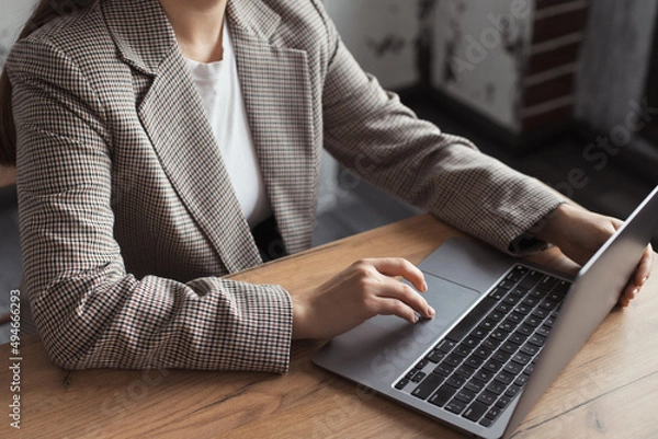 Fototapeta Woman hands typing on touchpad computer, working remote online. Faceless business woman working on laptop at workplace in a trendy modern office with the table
