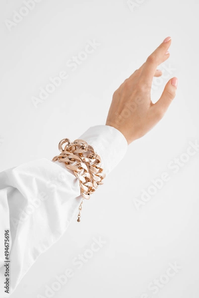 Fototapeta a woman's hand in a shirt with a gold bracelet on a white background, a beautiful palm on a white background (copy space)