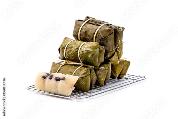 Fototapeta Pile of bundled boiled rice is stacked isolated on white background, Thai dessert made with glutinous rice and coconut milk put banana filling, wrapped in banana leaves and steamed until cooked.