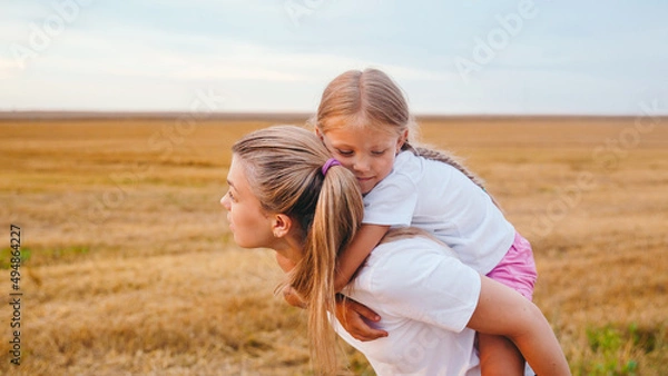 Obraz Young mother carrying her daughter on back outdoor