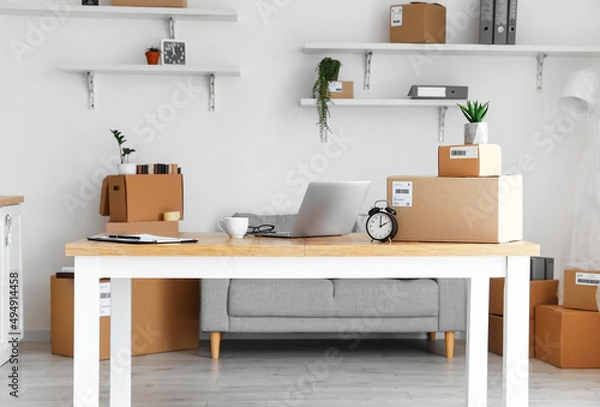 Fototapeta Cardboard boxes with belongings and furniture in interior of office on moving day