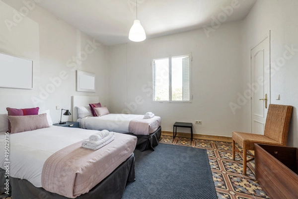 Fototapeta Bedroom with double beds with a set of white sheets and towels in a vacation rental apartment with hydraulic tile floors, blue carpet and white aluminum window