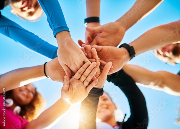 Fototapeta Gather around. Low angle shot of a group of young cheerful friends forming a huddle before a fitness exercise outside during the day.
