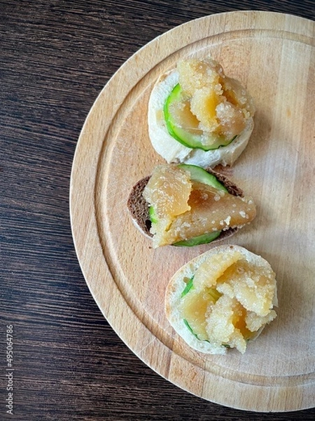 Fototapeta large vertical video. top view of a wooden board with small sandwiches. Herring caviar with cucumber slice on a piece of light and dark baguette. Source of omega-3. healthy snack. eco.