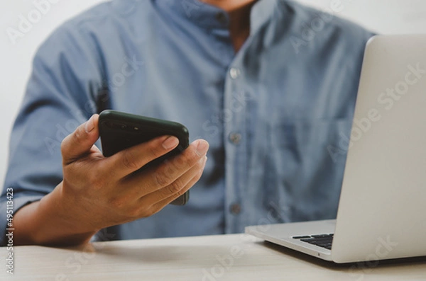 Fototapeta man using mobile smart phone and computer laptop searching internet, sending sms, using text messenger or online banking.