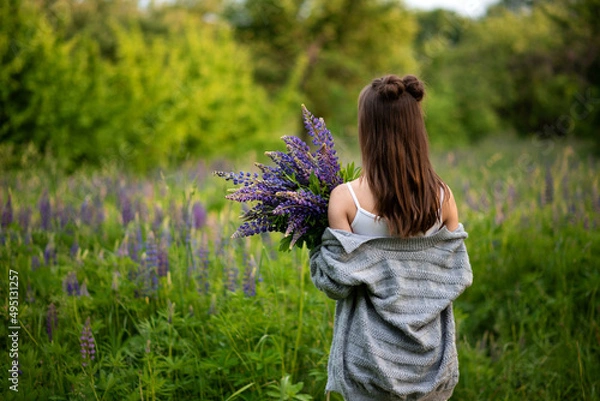 Obraz young beautiful girl holds in her hands spring lupine flowers and turned her back