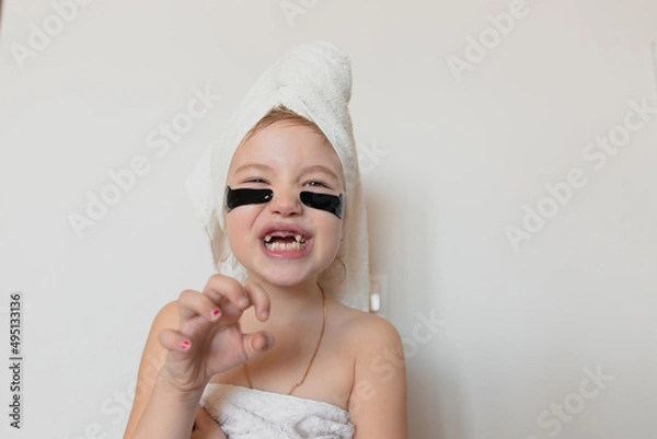 Fototapeta Portrait of a little girl after spa procedures with a towel on her head and with patches on her eyes ryaa like a tiger into the camera