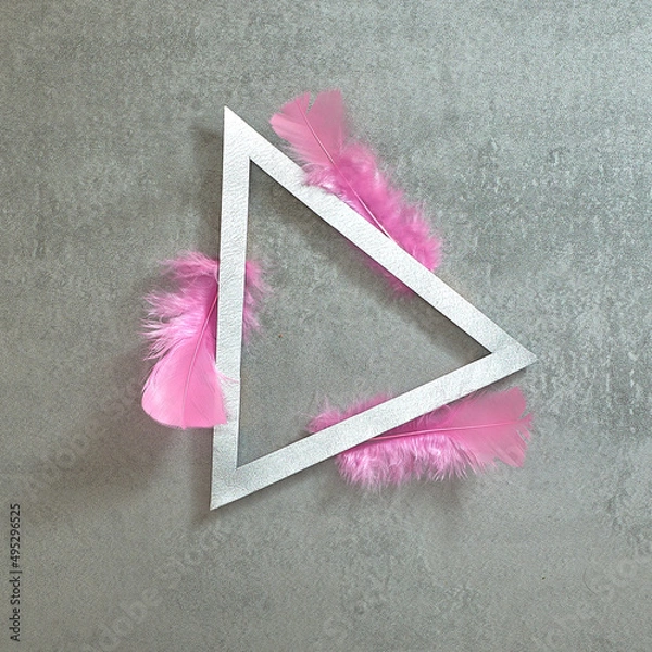Fototapeta Pink feathers around a silver triangular frame on a gray concrete background. Text space. Top view. Minimal style.