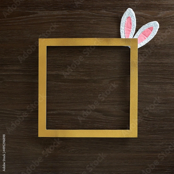 Fototapeta Gold frame with bunny ears in a corner, on a wooden background. Text space. Top view. Minimal style.