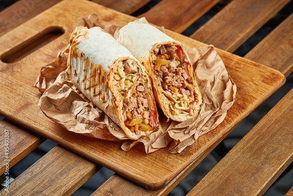 Fototapeta Large shawarma with meat and vegetables in kraft paper on a wooden background
