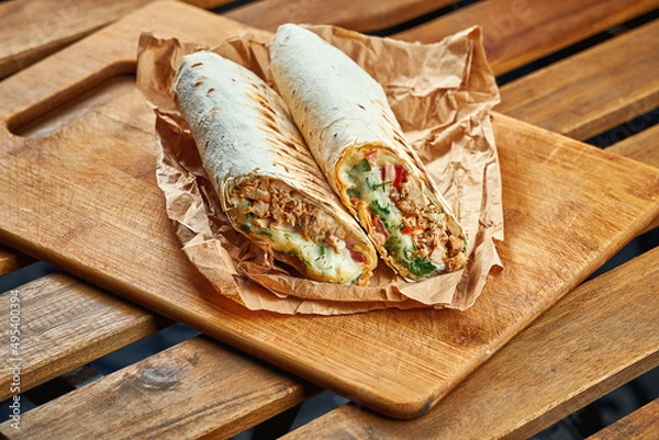 Fototapeta Large shawarma with meat and vegetables in kraft paper on a wooden background