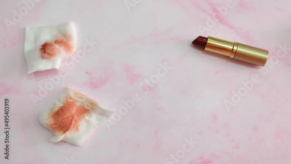 Obraz Two pieces of cotton pads with red stain from wiping off lipstick. With a tube of lipstick on the right.