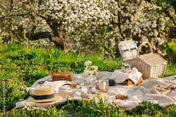 Fototapeta Breakfast picnic with waffles and tea in spring blossom garden on a white tablecloth on a sunny day, cherry blossoms. Outdoor, picnic, brunch, spring mood