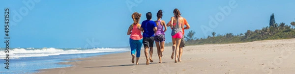 Fototapeta Panoramic view of friends jogging together on beach