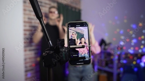 Obraz A guy and a girl dance on a smartphone camera. A view of the phone screen standing on a tripod. Social network. Blogger