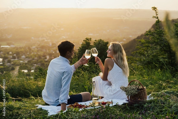 Fototapeta Romantic couple having happy on summer picnic, sitting on the hill, eating and drinking wine.