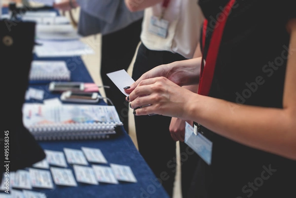 Fototapeta Process of checking in on a conference congress forum event, registration desk table, visitors and attendees receiving a name badge and entrance wristband bracelet and register electronic ticket