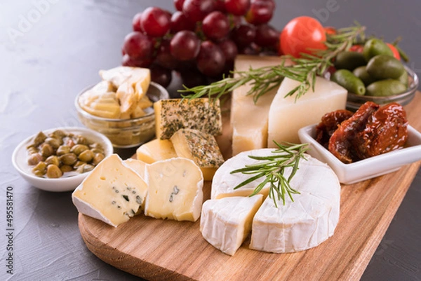 Obraz Charcuterie board with cheese. Assortment of antipasti - brie, blue cheese, gorgonzola, camembert, olives, cherry and sun dried tomatoes, artichokes, capers, grape. Cheese platter on gray stone table