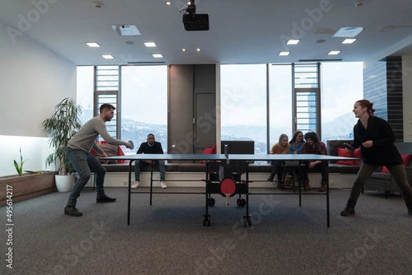 Fototapeta Young start up business man and woman playing table tennis at modern creative office space people group have meeting and brainstorming in background