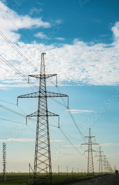 Fototapeta power lines along a highway at daytime with a cloudy deep blue sky