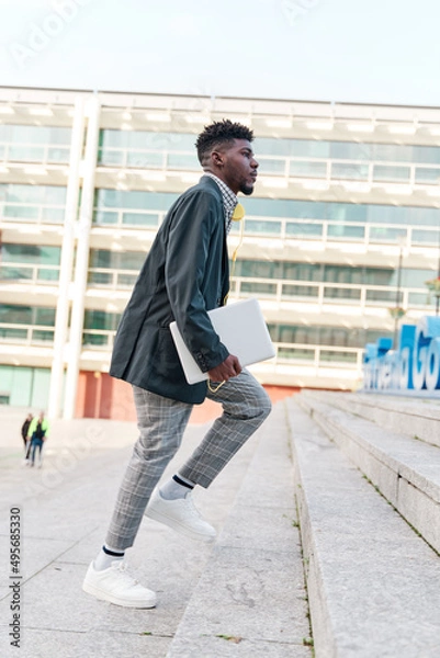 Fototapeta businessman walking up the stairs with a laptop in his hand and an office building behind him.