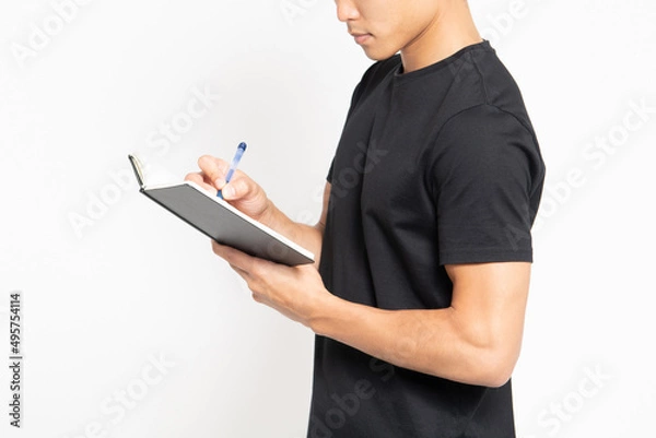 Fototapeta 白い背景の前に立ってノートに文字を書いている黒いTシャツを着ている男性