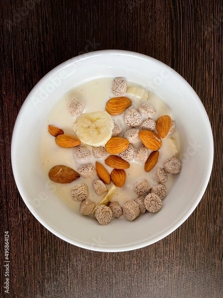 Fototapeta large vertical photo. homemade food. white yogurt with bran and slices of banana with almonds in a round ceramic plate with a pattern. useful vitamin breakfast. eco. bio. diet food.