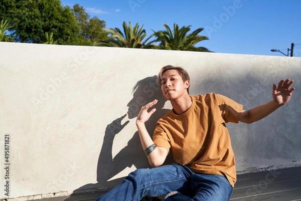 Obraz Man dancing touching chest by wall outdoors with trees and shadow profile