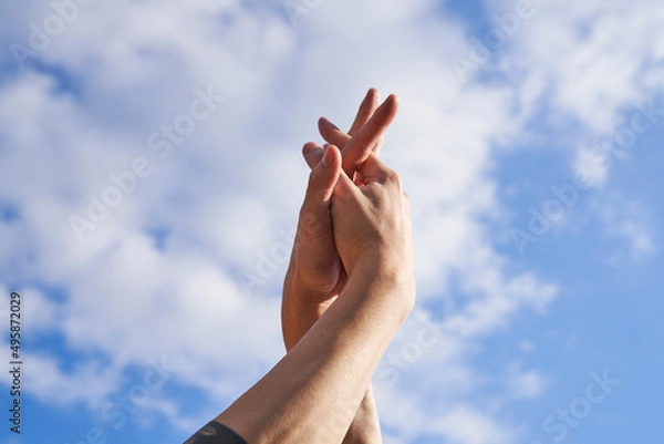 Obraz Hands with fingers crossed with partly cloudy sky