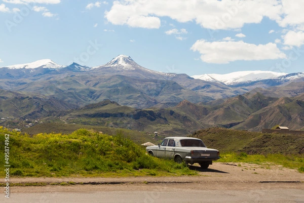 Fototapeta An old Soviet car stands on the roadside against the backdrop of snow-capped mountain peaks. Armenia