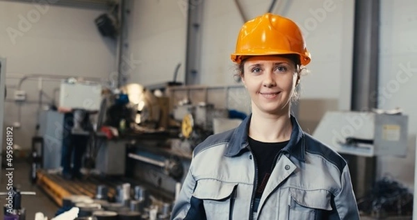 Fototapeta Portrait of a professional heavy industry engineer in uniform, goggles and a hard hat in a steel mill. Pretty industrialist woman standing at a metalwork facility.