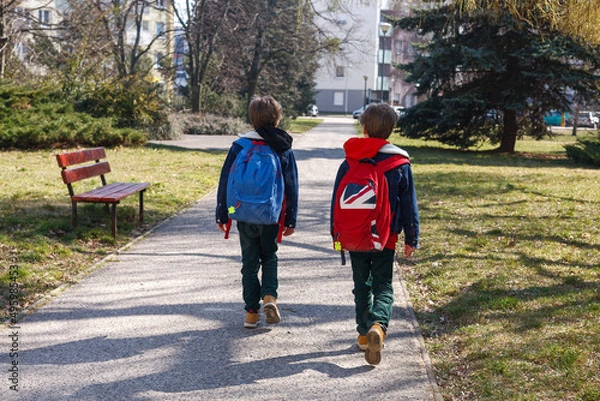 Obraz Dwoje dzieci spacerujących z plecakami do szkoły wzdłuż osiedla za aleja