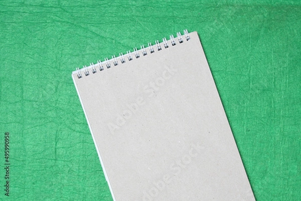 Fototapeta White and gray notepad sheet with spiral against the background of green fabric. Concept of analysis, study, attentive work. Stock photo with empty place for your text and design.