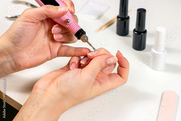 Fototapeta Young Caucasian woman making self manicure at home with the help of electrical fraser machine and other tools for nail procedures.