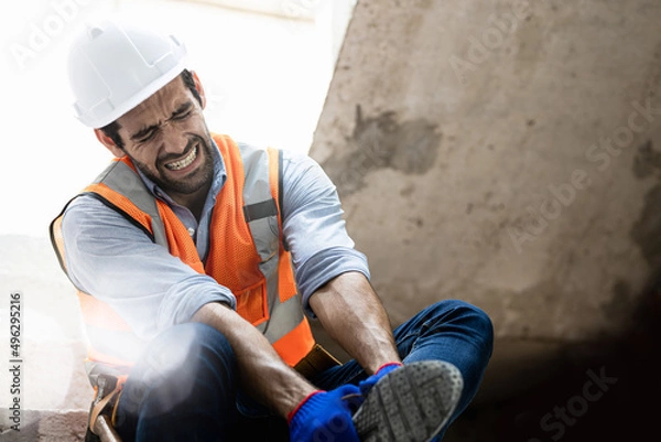 Fototapeta Handsome engineer injured his ankle when he stepped on a nail while inspecting a house project. Concept of occupational safety and occupational accident insurance.