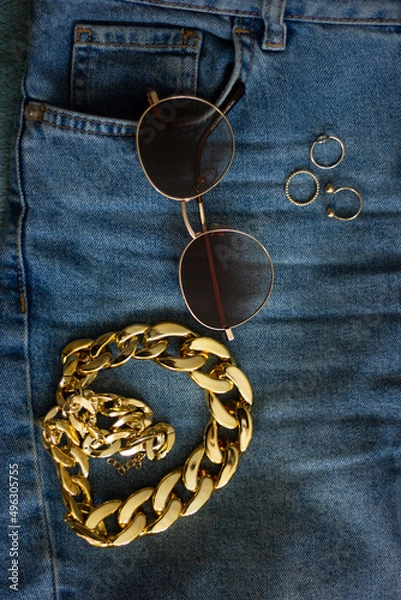 Obraz Gold chain, glasses and rings on jeans. Top view. Flat layout