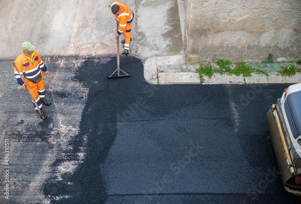 Obraz worker leveling fresh asphalt during asphalt pavement repair or construction works