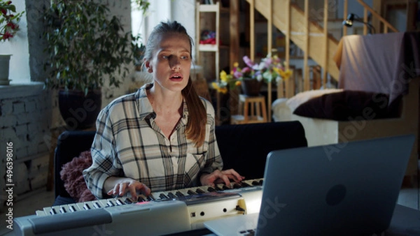 Fototapeta A woman starts playing the piano and communicates with a tutor via video link