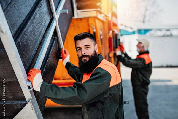 Obraz Senior and young garbage men working together on emptying dustbins for trash removal..