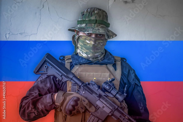 Fototapeta Angry russian soldier armed with a rifle with russia flag as background behind