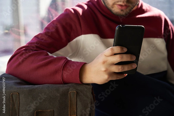 Obraz boy's hand resting on his backpack consults the mobile phone