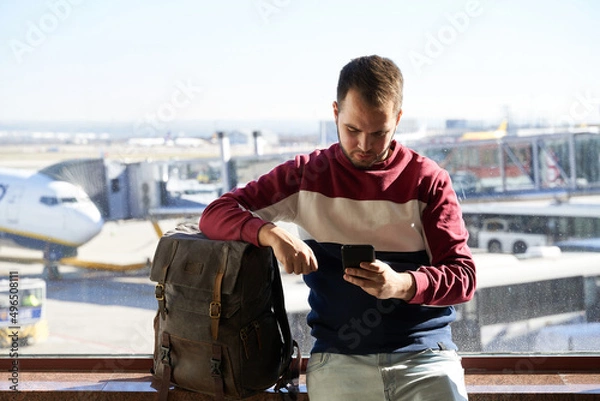 Obraz young man navigates with his phone while waiting for his flight to leave