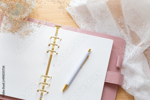 Fototapeta Flat lay, top view of a pastel pink leather planner, dried flower bouquet and stationery on a wooden desk.