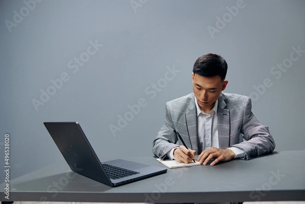 Fototapeta Asian man writing in a notebook laptop work at the desktop Gray background