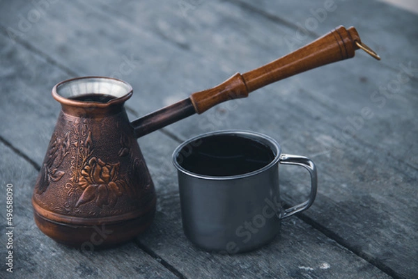 Fototapeta 
Copper cezve and a metal mug with coffee on a wooden table.