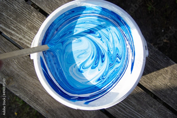Fototapeta white and blue paint is stirred in a bucket with a stick