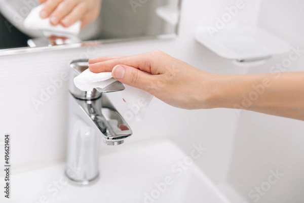 Fototapeta Cleaning the sink faucet with a microfiber cloth. Sanitize surfaces prevention in hospital and public spaces against corona virus. Woman hand using wet wipe. Cleaning the bathroom.