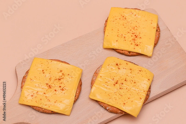 Fototapeta Crispy Cracker Sandwiches with Cheese and Paprika on Wooden Cutting Board and Beige Background